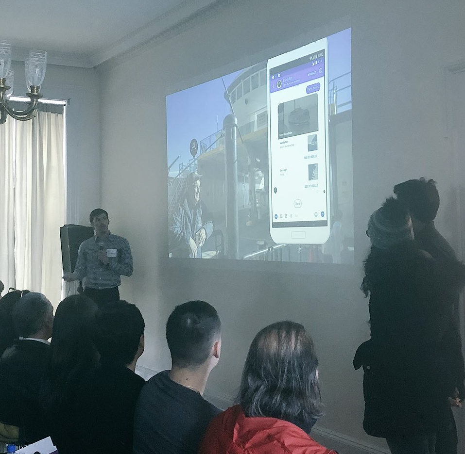 Two men and woman standing in front of a seated crowd presenting images on a projection screen