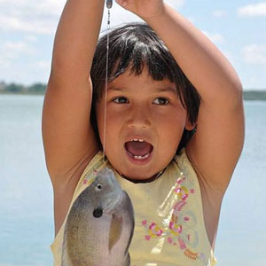 A young girl with a fish on the end of her line.