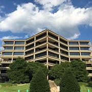 Image shows a multi-storied office building with trees and cloudy sky