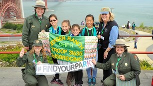 Girl scouts posing with park rangers and a sign reading 