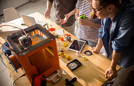 Three people standing around a small desktop 3D printer