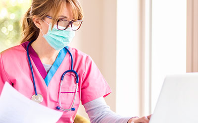 Nurse wearing a mask and working on her laptop