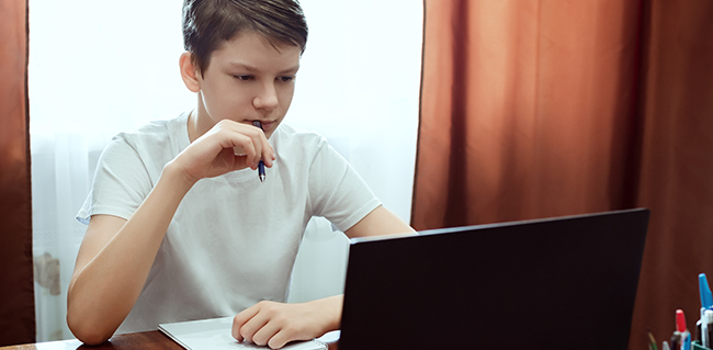 Student looking at computer, watching online education classes or webinar at home.
