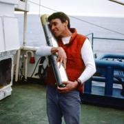 A man standing on the deck of a ship holds a core sample taken from the ocean floor.