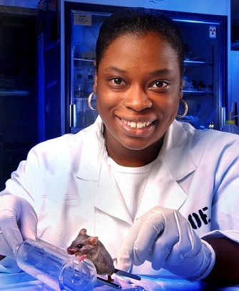 THIS STUDENT in a lab coat at Oak Ridge National Lab holds a plastic wheel that a mouse it standing on, ready to push. 