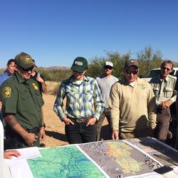 A group of people stand around a map laid out in the back of a truck while on a field trip.