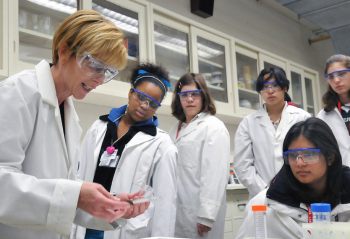 Group of scientists wearing lab coats and safety glasses, examining some items in a lab.