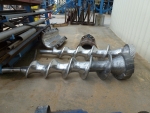 Two screw augers, one new (foreground) and one eroded (background), which was pulled from the machinery for rebuilding