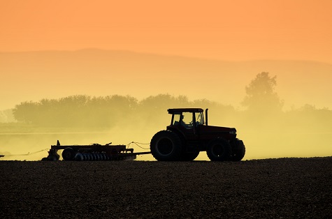 Tractor on field silhouetted against sunset sky