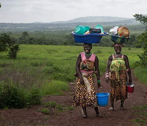 Two women from Guinea carrying children on their backs and balancing laundry dishes on their heads. Photo: Scott McPherson, RTI International