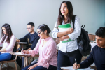 Students in a classroom taking notes, one student is standing up holding their books