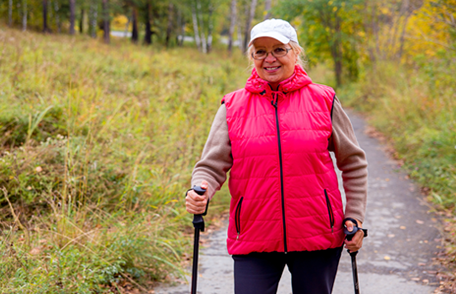 an older woman in a pink jacket hiking with the aid of hiking sticks
