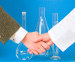 Photo of two hands in a handshake, with glass lab beakers behind them.