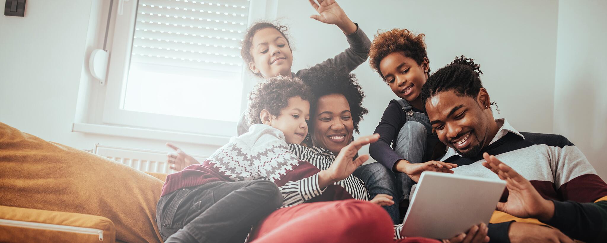 A family sits together on the couch looking at a tablet. 