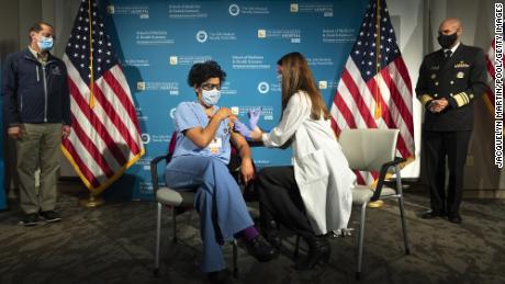 WASHINGTON, DC - DECEMBER 14: U.S. Health and Human Services Secretary Alex Azar (L) and U.S. Surgeon General Dr. Jerome Adams (R) watch as Dr. Sheetal Sheth, center left, OB-GYN and Medical Director for Labor and Delivery at George Washington University Hospital, is vaccinated for COVID-19 by nurse Lillian Wirpsza at George Washington University Hospital on December 14, 2020 in Washington, DC. Azar and Adams are observing hospital workers being vaccinated. (Photo by Jacquelyn Martin-Pool/Getty Images)