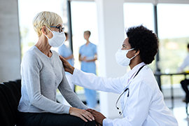 Black doctor and mature patient wearing protective face masks while talking in waiting room at clinic