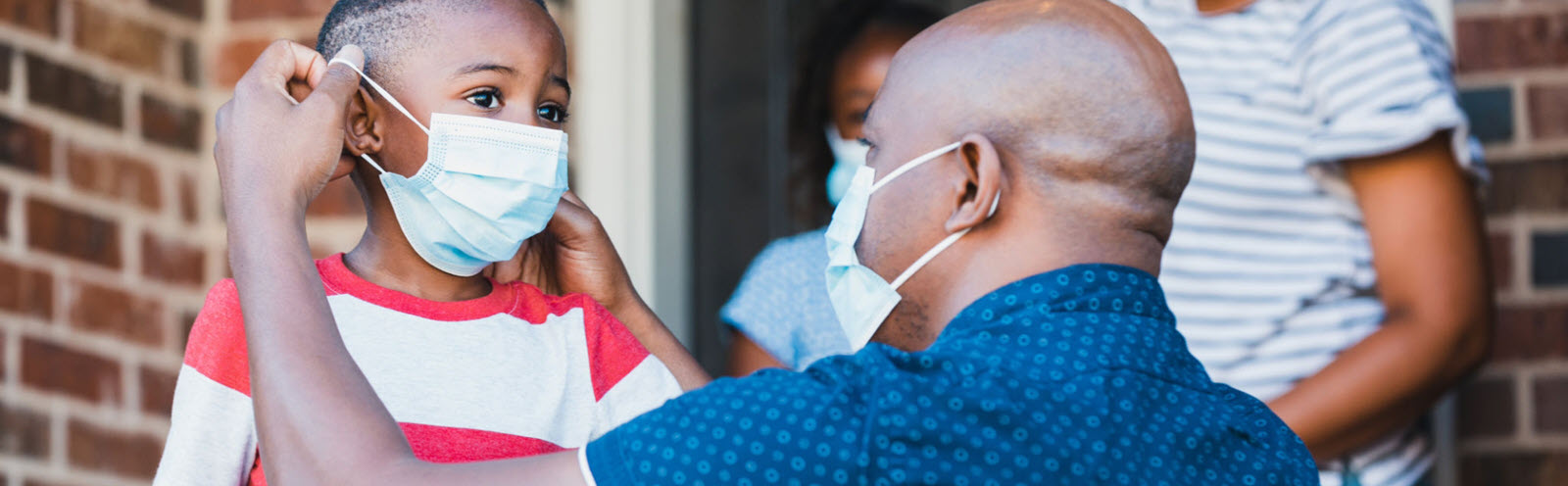 Father helping a young boy put on a face mask