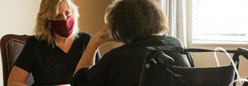 Female healthcare provider wearing a face mask talking to an elderly woman