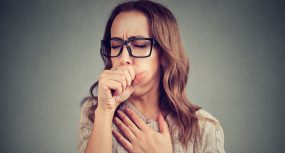 Photo of a woman coughing, covering her mouth with her fist and holding her chest.
