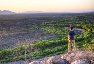 A hiker looks over San Pedro Riparian NCA with the sun shining across the landscape. Photo by Bob Wick.