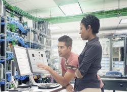 Photo of two people looking at computer screens in a server room