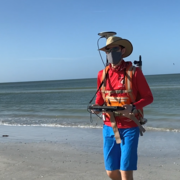 A man walks on a beach with a tablet in hand and a backpack on with scientific equipment extending from it. 