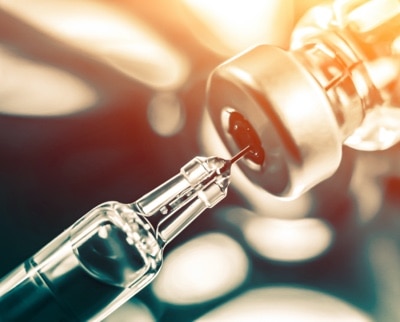 Syringe needle extracting the COVID-19 vaccine from a glass vial.