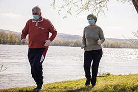 dos personas caminando al aire libre junto a un lago usando mascarillas de tela para la cara