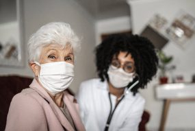 Bệnh nhân nữ cao tuổi ở nhà với nhân viên cung cấp dịch vụ y tế, cả hai người đều đeo khẩu trang