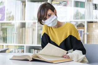 người phụ nữ đeo khẩu trang vải đang đọc sách trong thư viện
