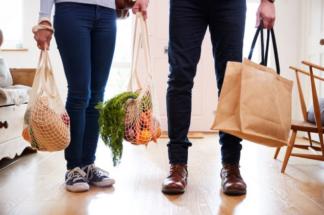 在外购物后回到家中的情侣特写图，手上拎着装满食品杂货的无塑料购物袋