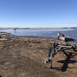 USGS technician stands next to a boat on a flooded and debris-filled landscape