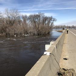 A USGS technician deploys a water measurement tool from a bridge to measure floodwaters