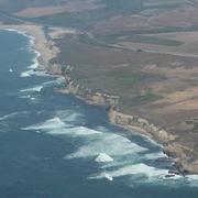 Aerial view of coastal bluffs, marine terrace with farmland, beach in distance with lagoon, highway runs along coast.