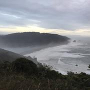 View from up high on a coastal cliff looking down along a beach where a river meets the ocean.