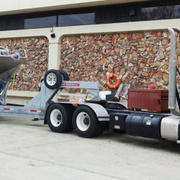 A large truck is parked near the wall of a building with a boat on the attached boat trailer.