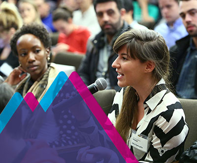 Female speaking into a microphone in a crowded auditorium