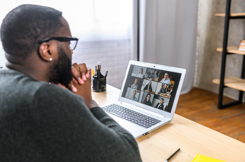 Man holding hands together while looking at laptop screen with other people displayed through webcam