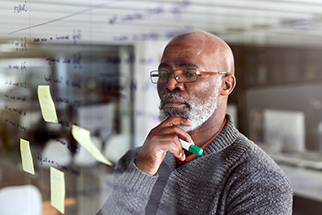 Mature Black businessman brainstorming with notes on a glass wall