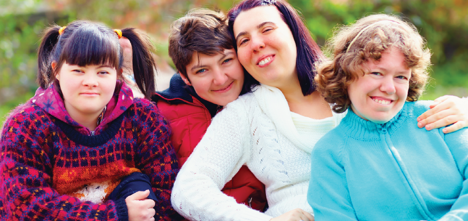 Four young women pose together smiling with trees in the background