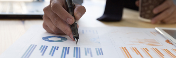 man writing on a printed chart with coffee in his hand