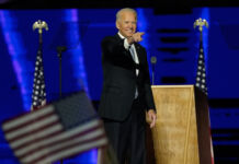 Joe Biden on stage, pointing, with U.S. flag in foreground (© Andrew Harnik/AP Images)