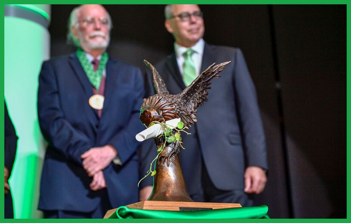 Photograph of bronze eagle statue in foreground with President Smatresk and previous award winner in background.